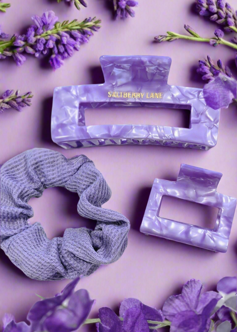 Komplettes Haarstyling-Set in Lavendel: Marmorierte Haarklammern und ein Scrunchie aus weichem Stoff, dekorativ mit violetten Blumen auf einem hellen Hintergrund – perfekte Kombination für trendige Frisuren.