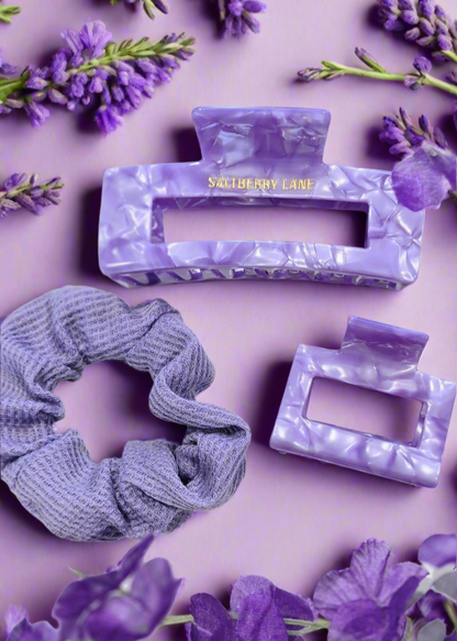 Komplettes Haarstyling-Set in Lavendel: Marmorierte Haarklammern und ein Scrunchie aus weichem Stoff, dekorativ mit violetten Blumen auf einem hellen Hintergrund – perfekte Kombination für trendige Frisuren.