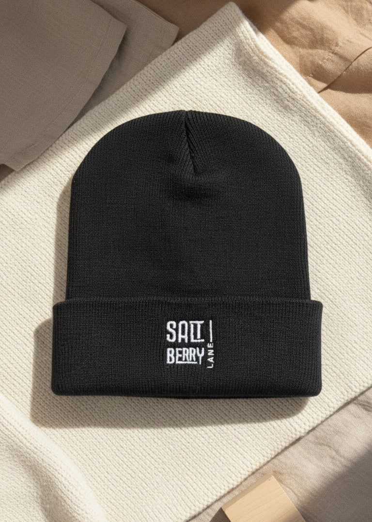Schwarze Saltberry Lane Beanie mit weißem gesticktem Logo auf Holzuntergrund, stylische limitierte Wintermütze für Damen und Herren.